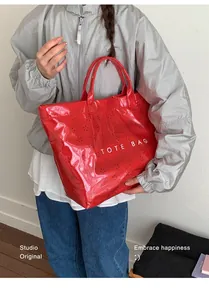 Détail d'un cabas en cuir verni rouge avec motifs ajourés et lettrage blanc