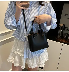Schicke schwarze Umhängetasche aus Leder mit Knotengriff am gestreiften Shirt-Modell