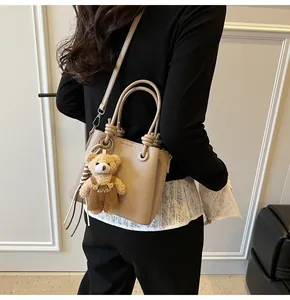 Beigefarbene Handtasche aus Litschi-Leder mit Bärenanhänger an der Schulter