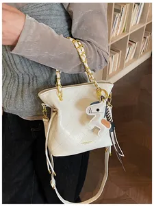 Detail of white quilted tote bag with gold chain and leather horse charm on a model