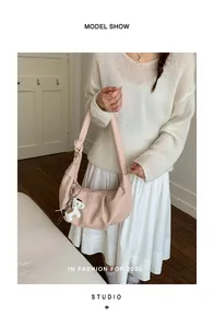 Detail of light pink croissant shoulder bag featuring a decorative horse charm and knotted strap