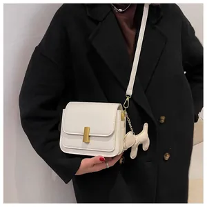 Detail van witte leren crossbodytas met gouden gesp en een schattige hondenhanger