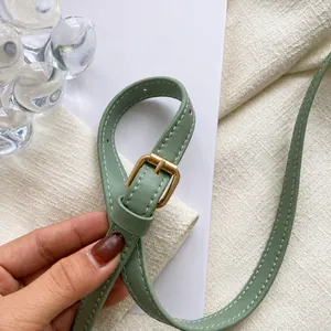 Detail of light green leather shoulder strap with adjustable golden buckle and punch holes