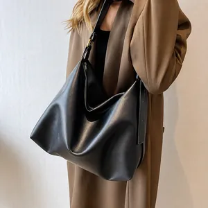 Minimalist black hobo bag with adjustable strap worn by model in a stylish trench coat