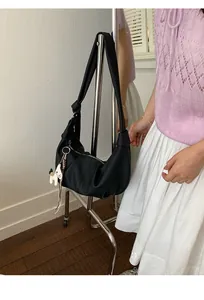 Detail of black pebbled leather hobo bag with wide shoulder strap and white horse charm