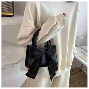 Close-up of black handbag featuring a large silk-like bow and durable rolled handles