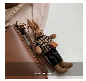 Detailed close-up of a brown plush rabbit charm with houndstooth vest on a leather tote bag