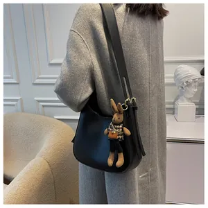 Detail of minimalist black leather crossbody bag with a cute rabbit charm and gold buckle