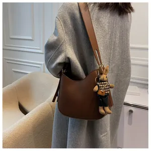 Detail of a brown leather hobo shoulder bag with a cute rabbit plush charm and wide strap