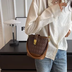 Sac seau marron tressé avec serrure dorée et double bandoulière porté par un mannequin