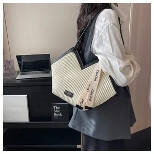 Detail of a pleated canvas tote bag in off-white with black straps and side ribbon detail