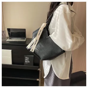 Detailed view of black pleated tote bag with branded canvas shoulder strap in an office setting