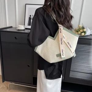 Minimalist cream pleated canvas tote bag with green trim shown on a model in a cafe