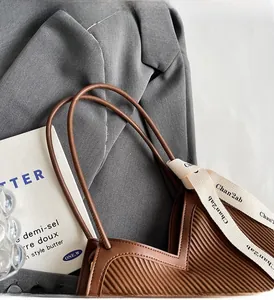 Macro shot of brown pleated tote bag featuring thin leather handles and stylish logo ribbon