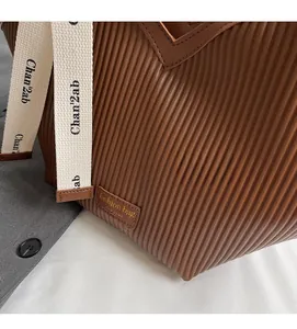 Detail of coffee brown pleated tote bag with branded fabric strap and leather patch logo