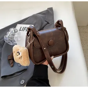 Detail view of dark brown retro crossbody bag with adjustable strap and bear pendant