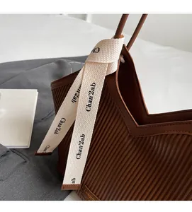 Close-up of brown textured tote bag with pleated leather and decorative ribbon detail