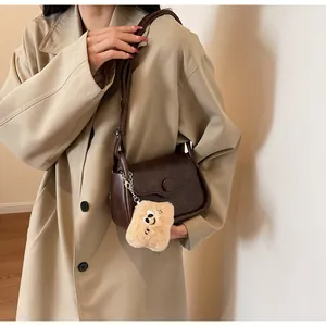 Detail of dark brown retro crossbody bag featuring a cute beige plush biscuit pendant