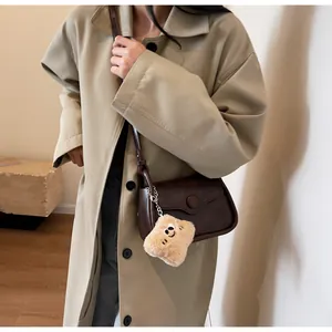 Detail view of a dark brown crossbody bag featuring a cute beige plush square charm