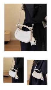 Détail d'un sac à main blanc en cuir semi-circulaire avec pendentif monstre en peluche
