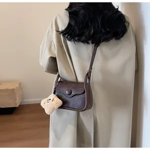 Detail view of dark coffee retro crossbody bag with round buckle and plush charm