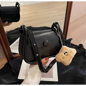 Detail view of black faux leather handbag featuring a plush smile charm and adjustable strap