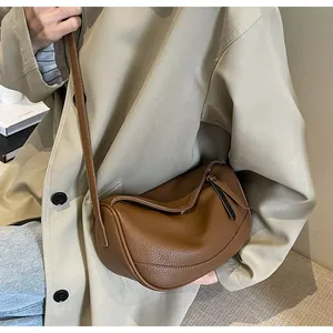 Brown lychee leather crescent bag shown crossbody on model in casual beige trench coat
