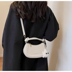 Gros plan du sac demi-lune crème avec pendentif monstre en peluche sur mannequin