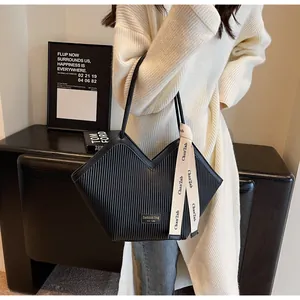 Detail of black pleated tote bag with V-shaped opening and decorative ribbon accent