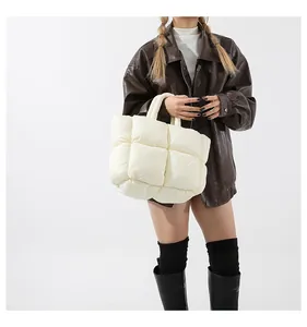Detail of a padded white quilted tote bag worn by a model in a brown leather jacket