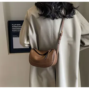 Side view of a brown pebbled leather half-moon crossbody bag on a beige trench coat