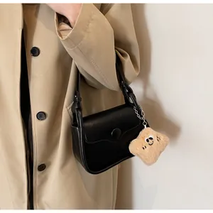 Close-up of black leather crossbody bag with minimalist flap and cute plush toast pendant