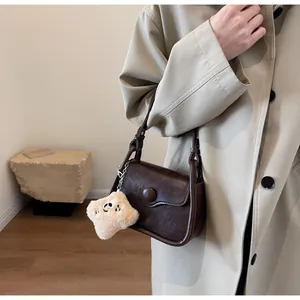 Retro brown leather crossbody bag with cream plush charm shown on person