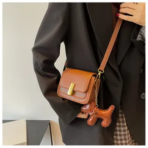Détail de la sacoche en cuir marron avec boucle dorée et pendentif décoratif en forme de chien