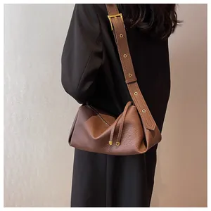 Detail of a brown leather shoulder bag with lychee texture and gold metal eyelet strap
