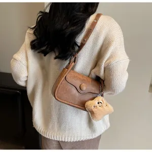 Close-up of a brown retro crossbody bag with a plush star charm on a white sweater