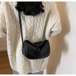 Detail shot of a black litchi grain leather crossbody bag styled with a knit sweater
