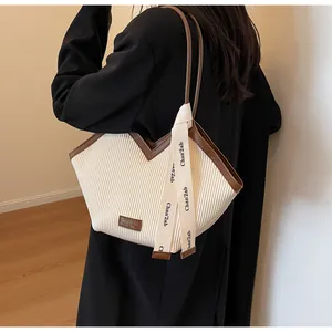 Detail of pleated beige tote bag with brown trim, logo patch and decorative ribbon