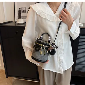 Detail of grey bucket bag with checkerboard handle and plush charm on white shirt