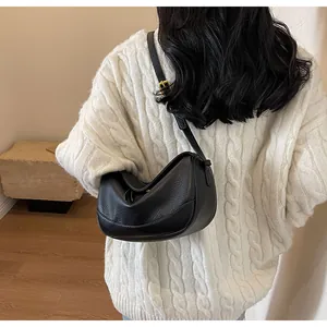 Close-up of black lychee grain leather crossbody bag worn with a white knit sweater