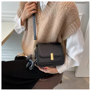 Détail du sac bandoulière noir avec boucle dorée et breloque chien sur tenue beige