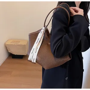Detail of brown pleated tote bag featuring vertical texture and a decorative white ribbon