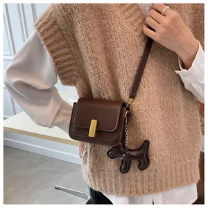 Détail du sac bandoulière marron foncé avec boucle dorée et breloque chien mignonne