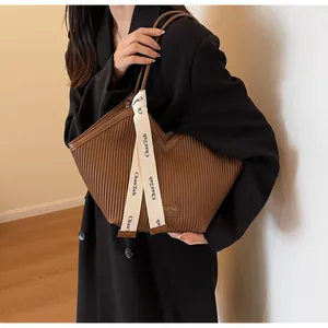 Detail of brown pleated tote bag with branded ribbon handle and modern PU leather texture