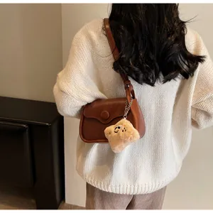 Close-up of brown retro shoulder bag with glossy finish and cute plush charm pendant