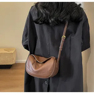 Brown litchi leather shoulder bag with gold hardware shown on person with black coat