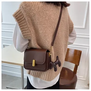 Détail du sac à bandoulière en cuir marron foncé avec boucle dorée et breloque chien