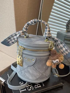 Blue cylindrical bucket bag with silk scarf handle and plush pendant on black book