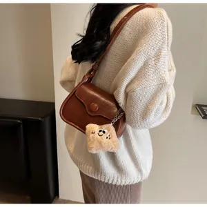 Detail view of a brown vintage crossbody bag with large round buckle and plush smiley pendant