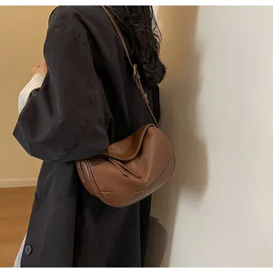 Detail of a brown pebbled leather crescent crossbody bag shown on model with shoulder strap